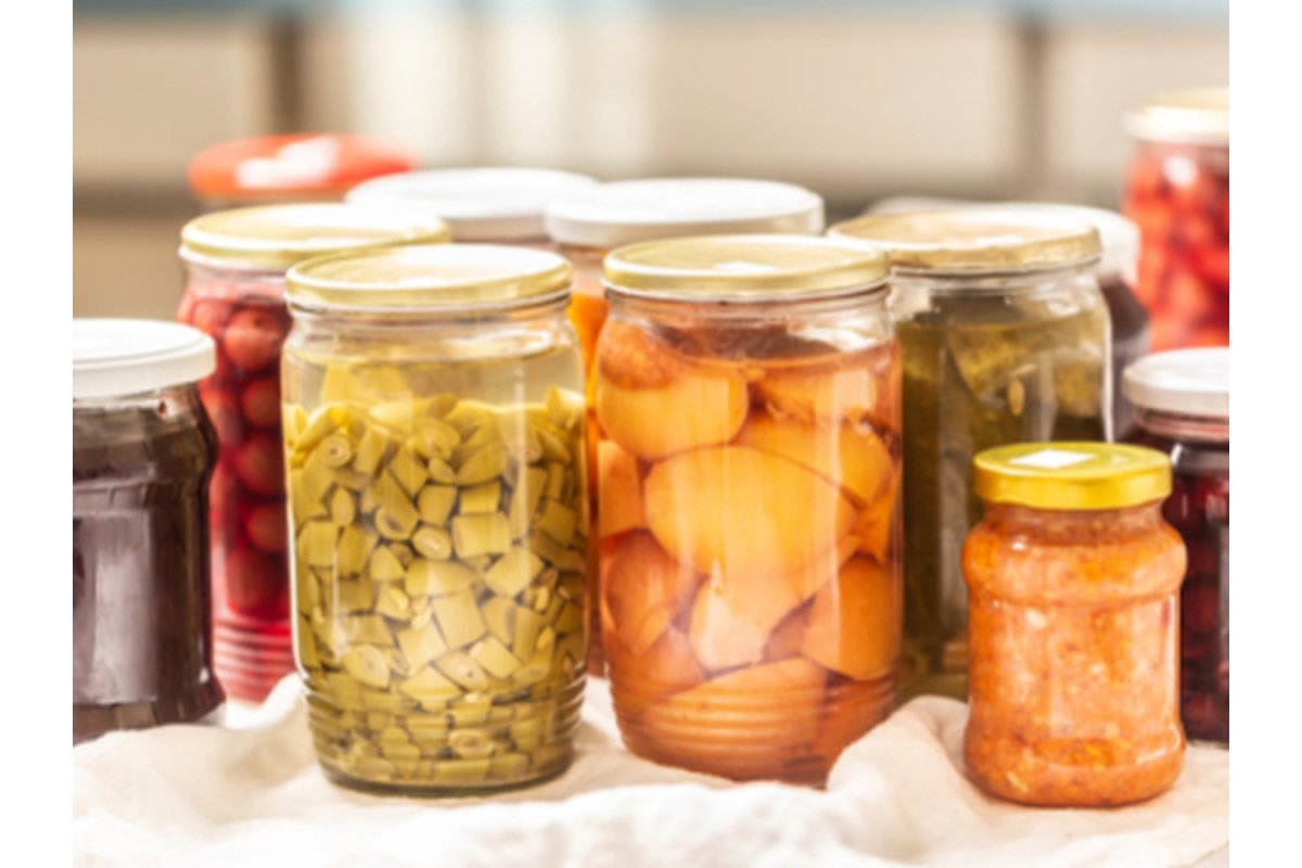 Barattoli di vetro con verdure estive sott'olio su un tavolo di legno.
