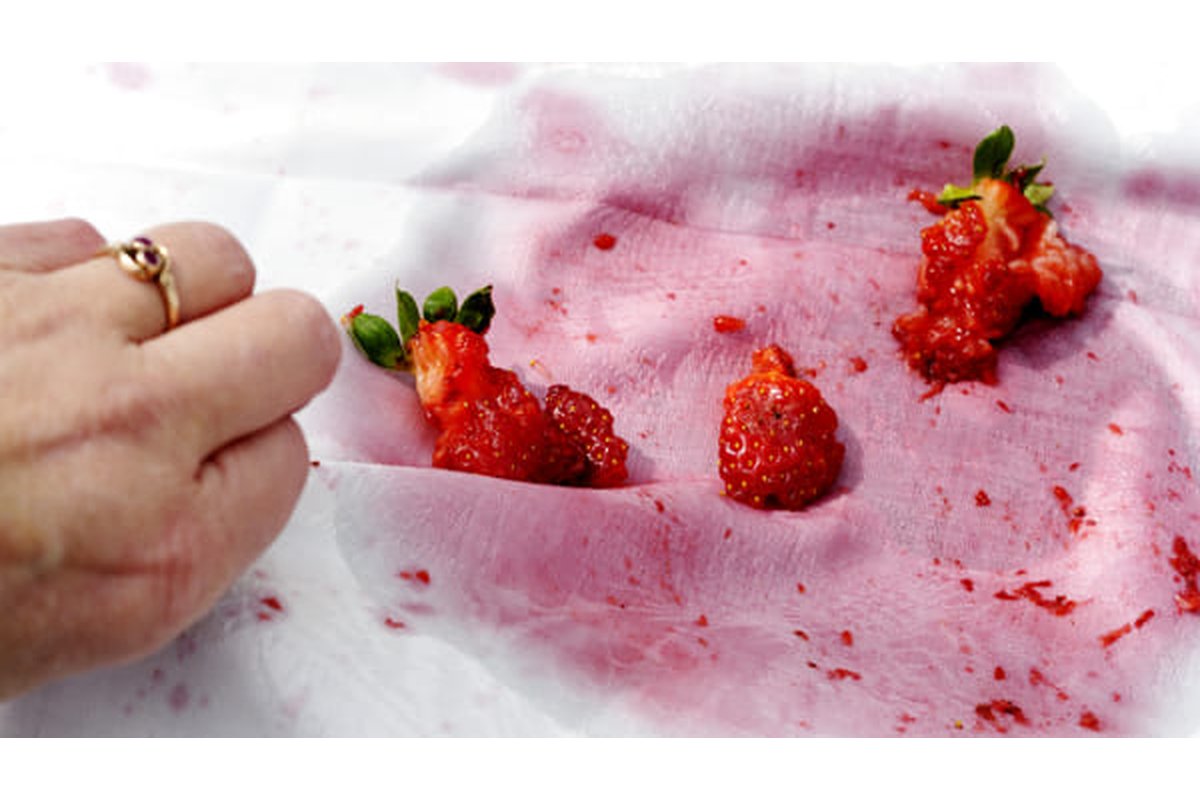 Macchia di fragola su tessuto bianco con prodotti per la pulizia accanto.