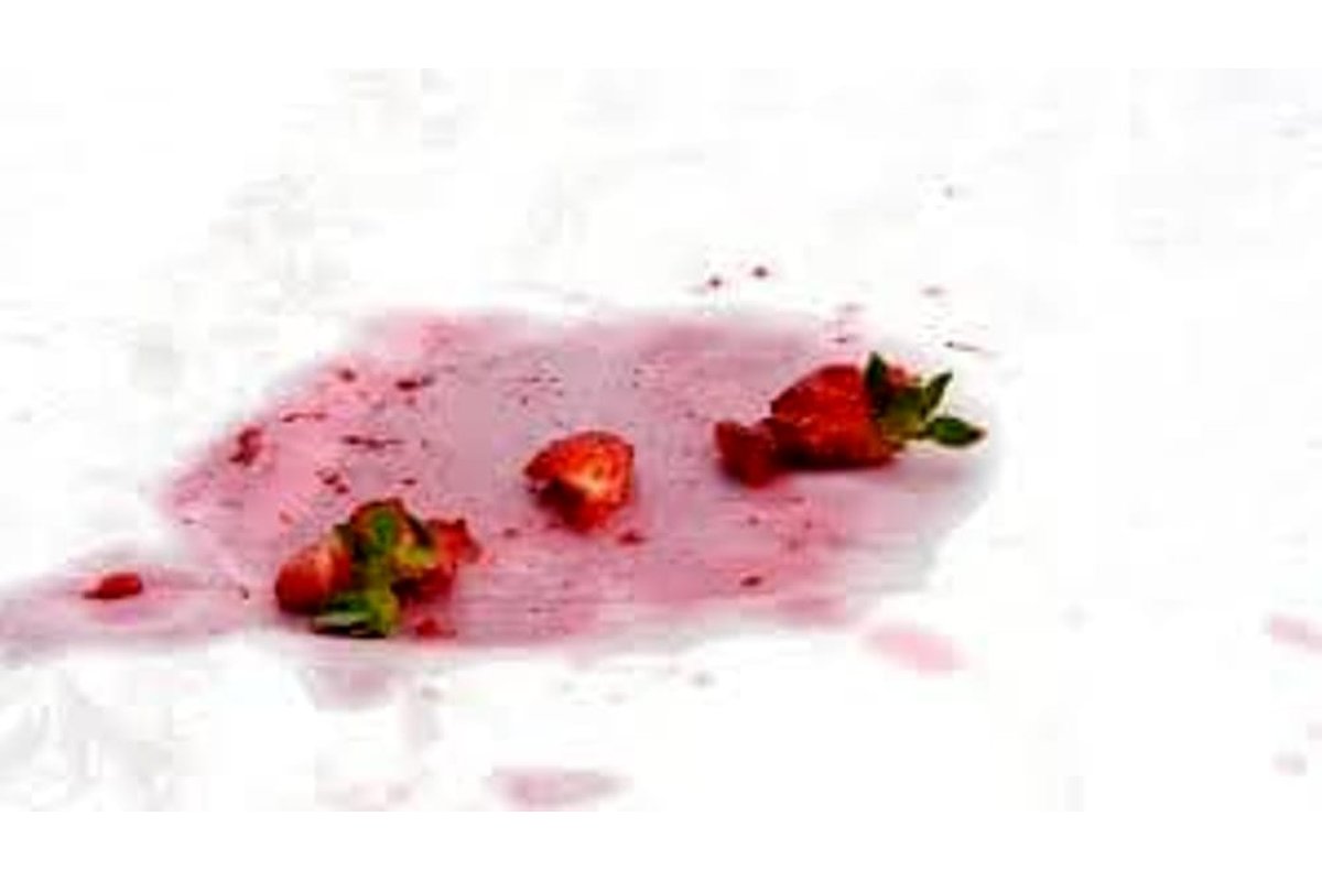 Mani che trattano una macchia di fragola su un tessuto bianco.