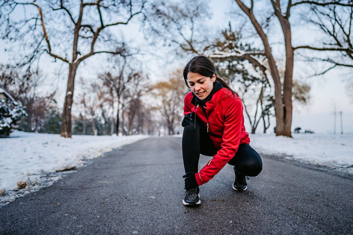 Persona con sciarpa che si massaggia il ginocchio dolorante in una giornata invernale.