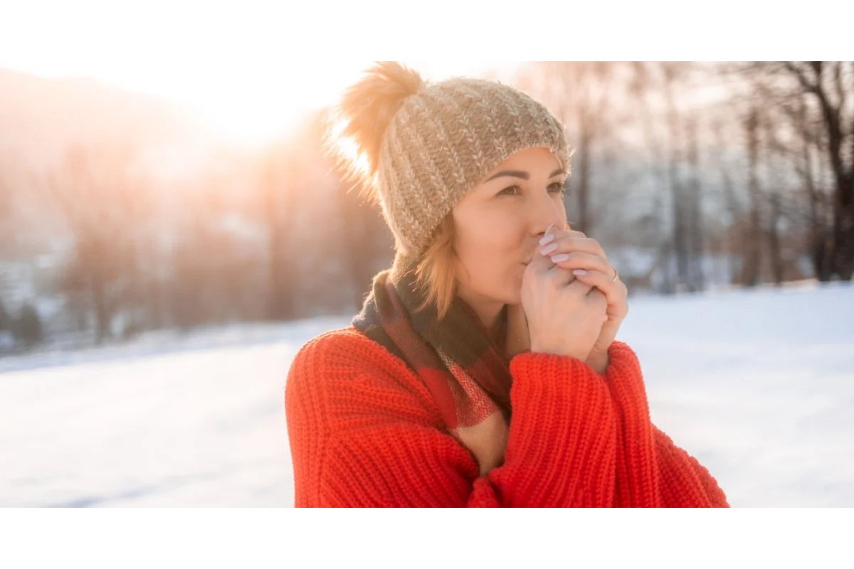 Persona con sciarpa e cappotto si tiene il ginocchio dolorante.