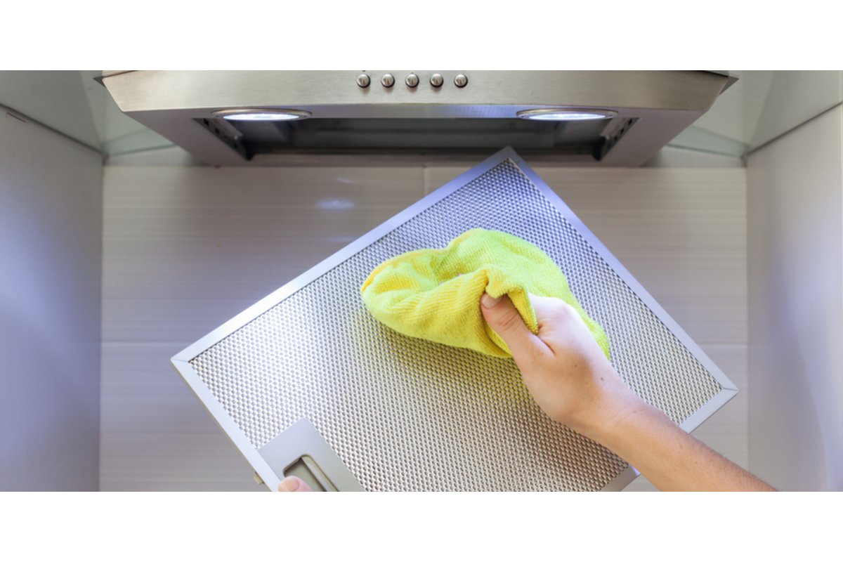 Mani che puliscono una cappa con un panno e un detergente naturale.