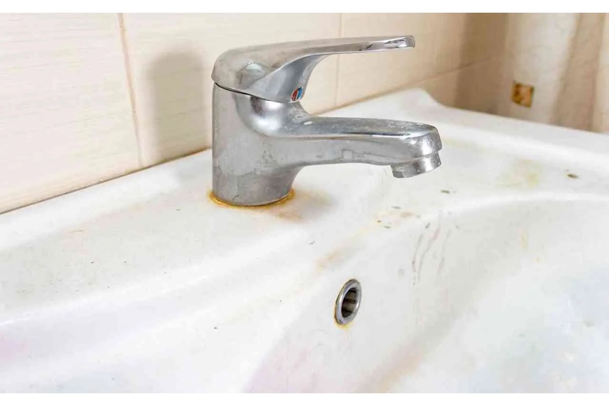 Mano che pulisce un lavabo con un panno bianco.